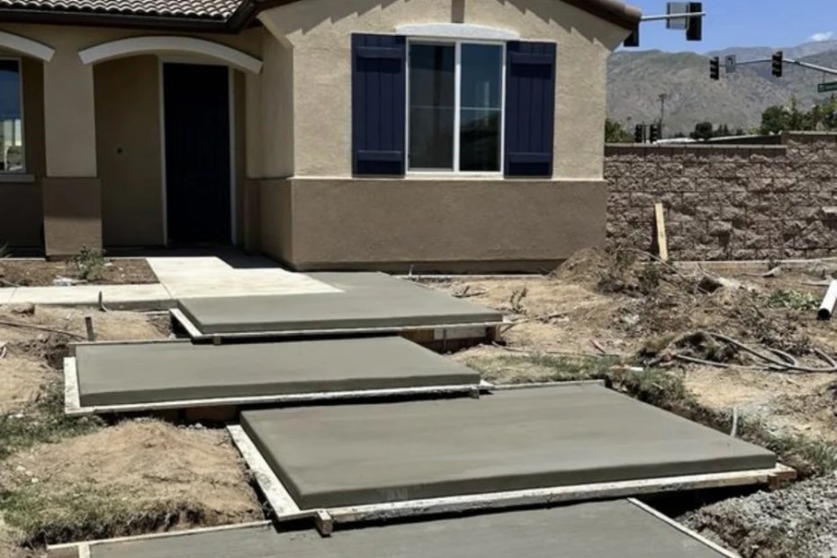 Freshly poured concrete walk pads in wood forms leading to a new stucco house