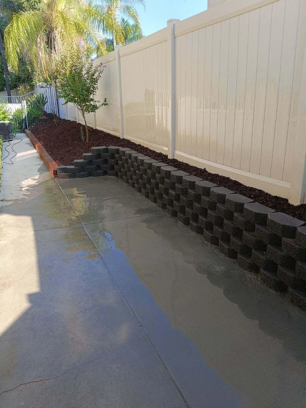 Low block retaining wall with fresh concrete and a mulched planting bed along a vinyl fence in Orange County, California