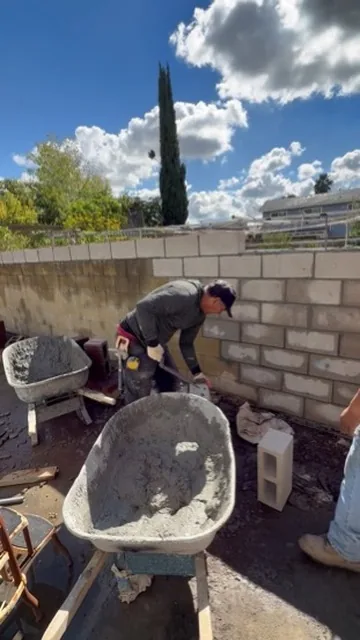 Crew member mixing mortar in a wheelbarrow beside a part built block wall in Orange County, California