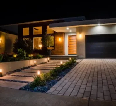 Paver entry walkway lit by low voltage path lights at dusk beside a poured concrete drive in Orange County, California