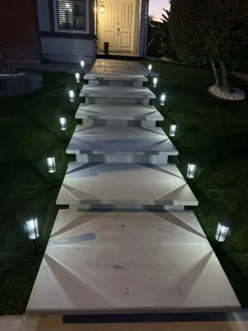 Low-voltage path lights along a concrete walkway at dusk with turf either side in Orange County, California