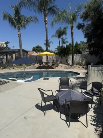 Pool patio with umbrella shade and mature palms behind a block wall in Orange County, California