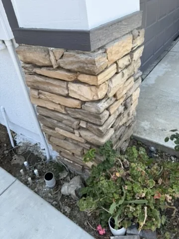 Stacked stone veneer column at the corner of a stucco house beside a poured walkway in Orange County, California