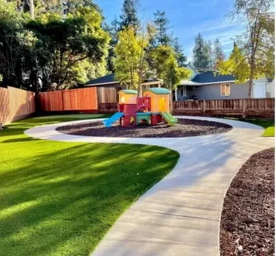 Curved artificial turf lawn wrapping a play structure with mulch beds behind in Orange County, California